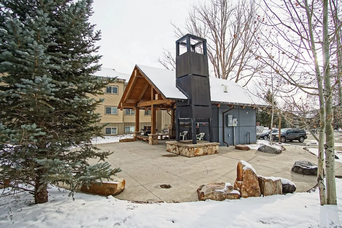 An outdoor seating area beneath a black tower structure and wooden overhang, with views of the winter scenery and a cozy fire pit. The area invites guests to gather, relax, and enjoy the outdoors.