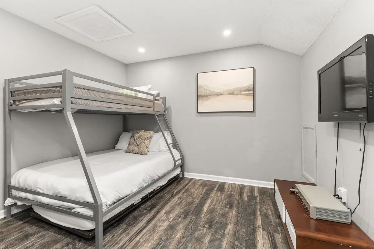 A comfortable sleeping space featuring a twin-over-full bunk bed, TV, artwork, and a wooden dresser. The layout is inviting for children or singles, offering both entertainment and restful sleep.