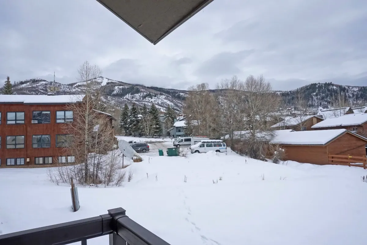 A scenic view of snow-covered mountains, a wooden building, and a snowy landscape framed by trees. The scene feels serene and captures the natural beauty of Steamboat Springs in winter.