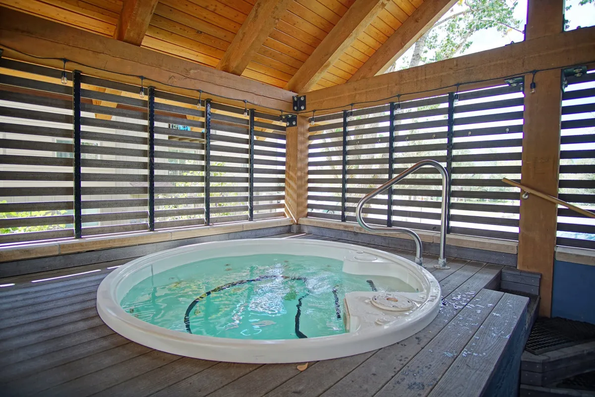 A tranquil hot tub setting featuring wooden beams and slatted windows, allowing natural light to filter in. The space is inviting for relaxation, with the promise of a soothing soak surrounded by nature.