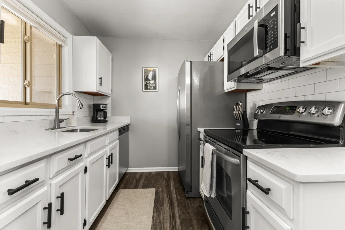 Another angle on a fully appointed kitchen with stainless steel appliances, white cabinetry, deep sink, and generous countertop space. The design is both functional and stylish, providing all the essentials for home-cooked meals and easy entertaining.