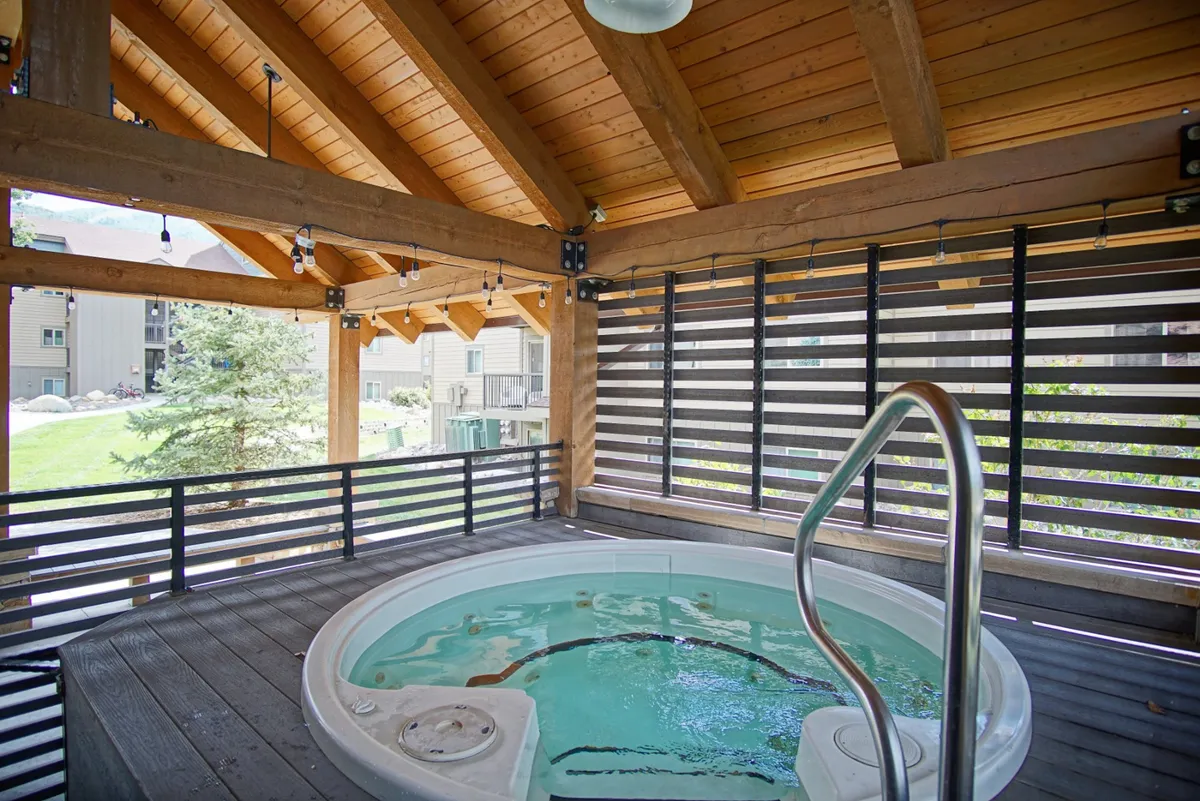 An inviting outdoor hot tub under wooden beams, surrounded by natural elements, with open views creating a serene atmosphere. The scene hints at relaxation and socializing after active days outdoors.