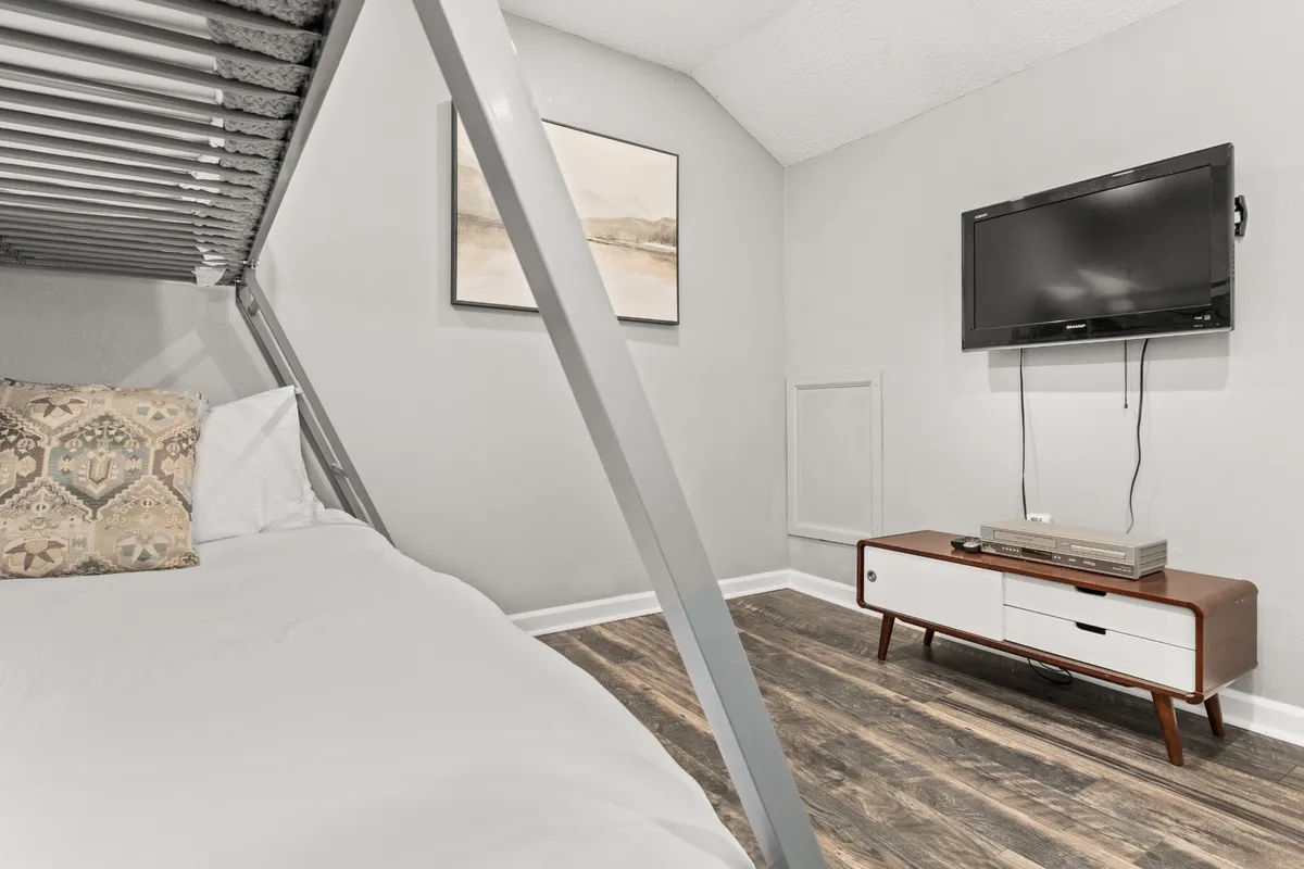 A contemporary loft area with a lofted bed frame, television, wooden media console, and chic wall art. The design is open and inviting, ideal for a flexible sleeping arrangement or private retreat.