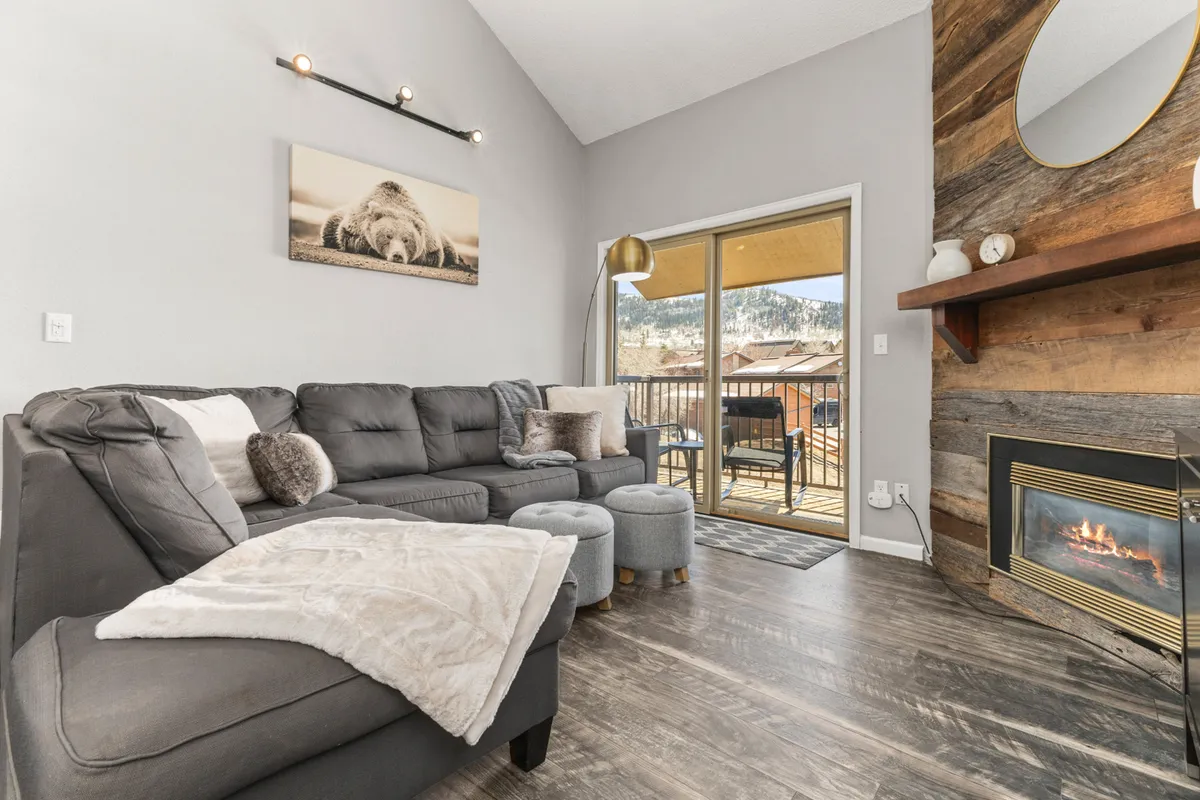 The image showcases a beautifully renovated living area with a plush sofa, a glowing fireplace, large window framing mountain views, and tasteful artwork, creating a warm and inviting space ideal for relaxation and gathering.